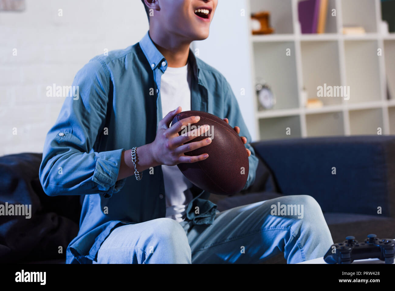cropped shot of smiling young man holding rugby ball and watching sport match at home Stock Photo