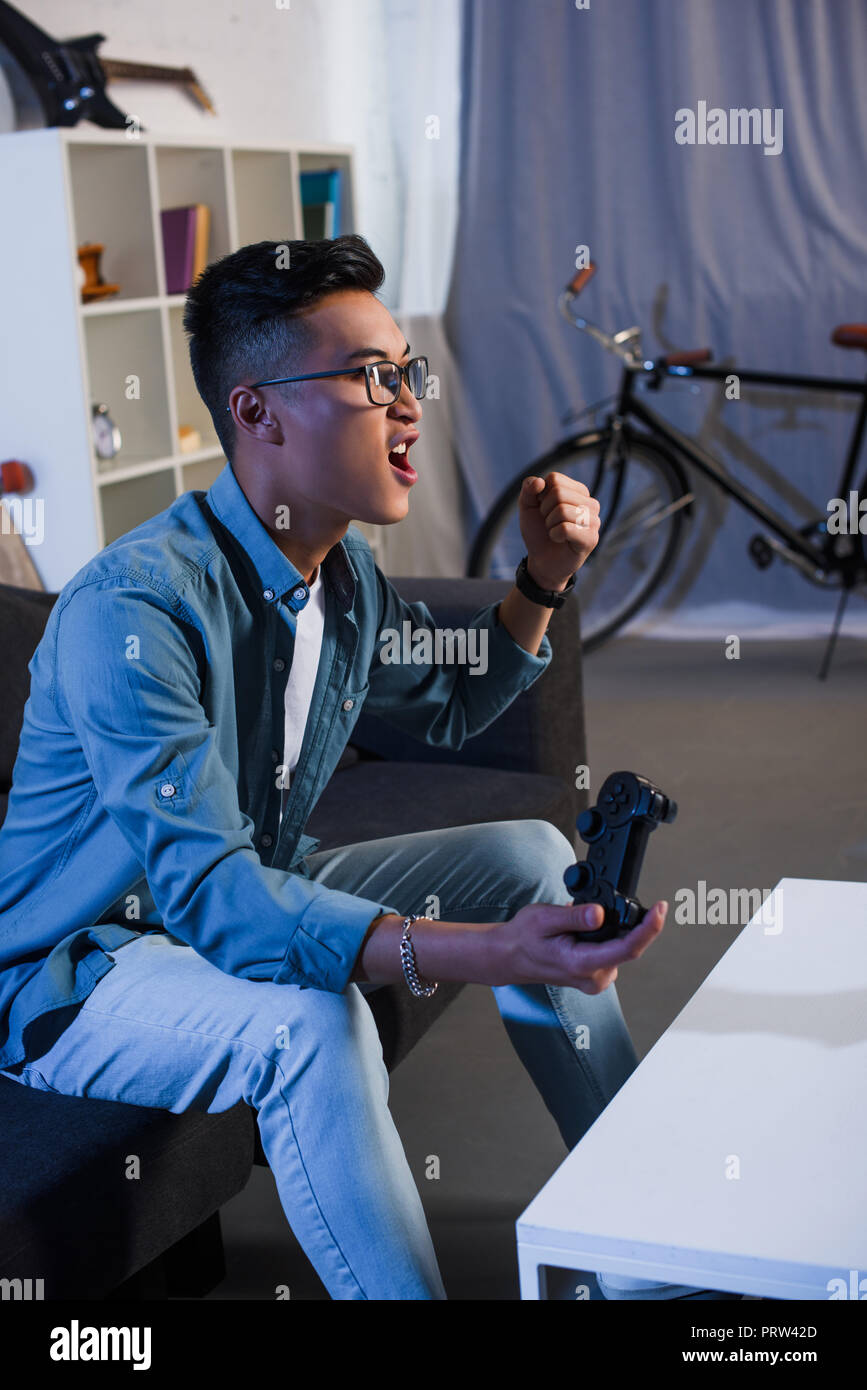 excited young asian man playing video game with joystick and win at home Stock Photo