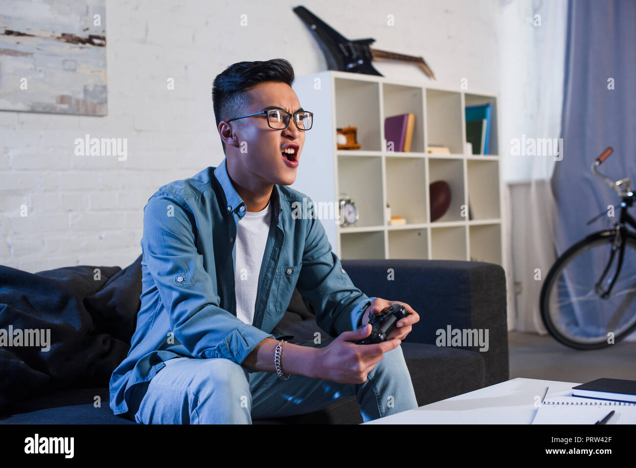 excited young asian man yelling and playing video game with joystick at home Stock Photo