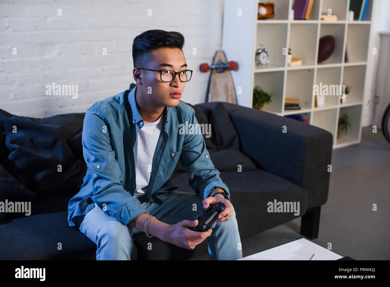focused young asian man playing video game with joystick at home Stock Photo