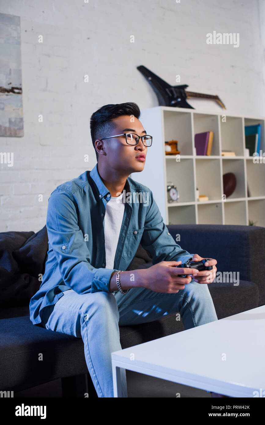 young asian man using joystick and playing video game at home Stock Photo