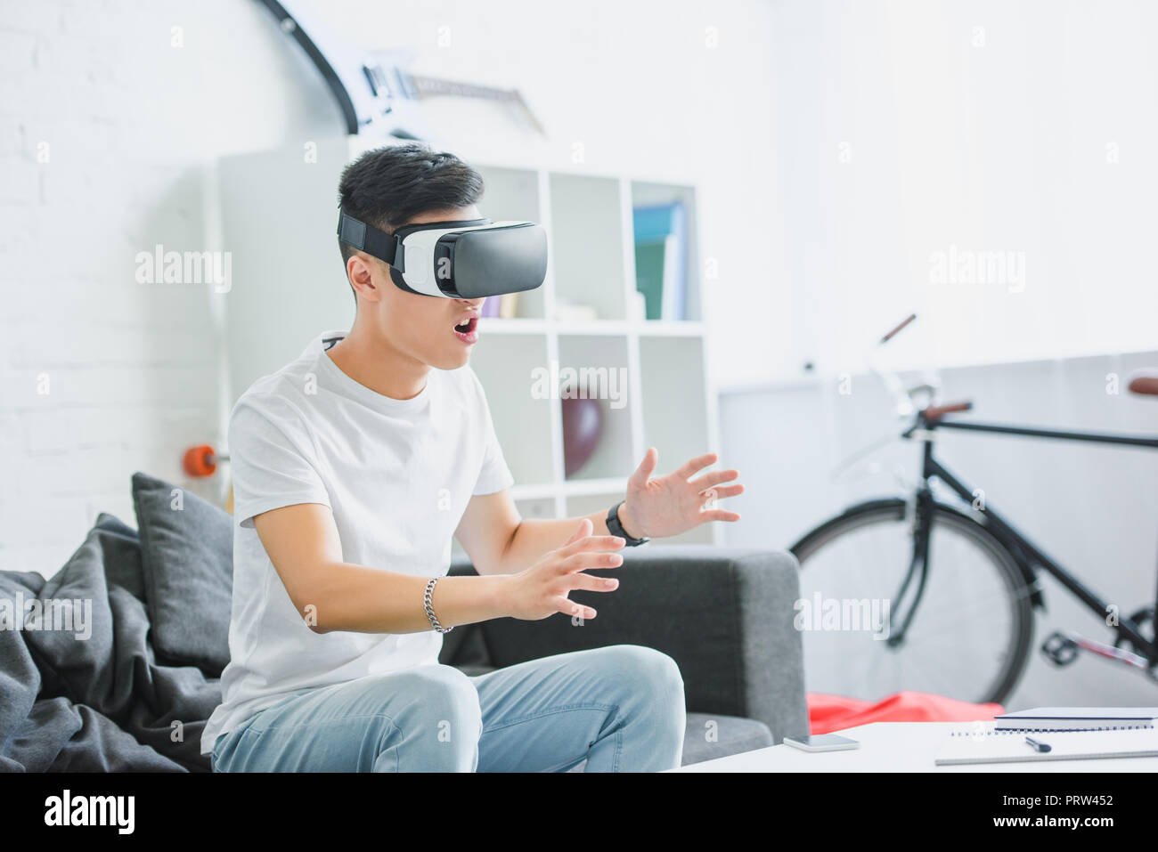 emotional young asian man sitting on couch and using virtual reality headset Stock Photo