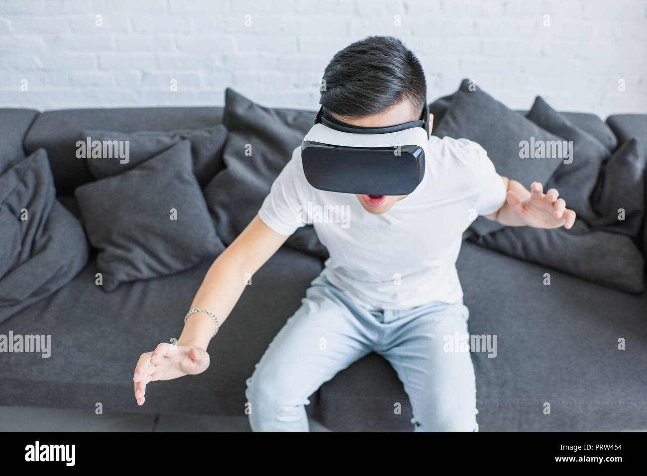 high angle view of emotional young man sitting on couch and using virtual reality headset Stock Photo