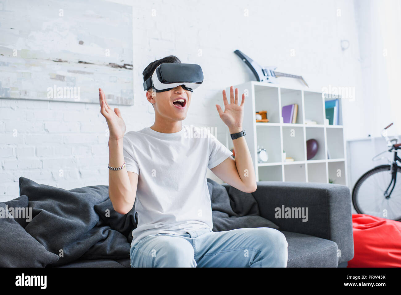 happy young asian man sitting on couch and using virtual reality headset at home Stock Photo