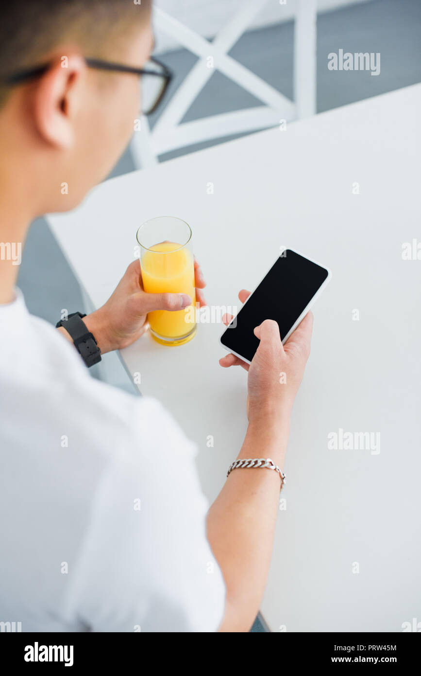 cropped shot of young man holding glass of juice and using smartphone with blank screen Stock Photo