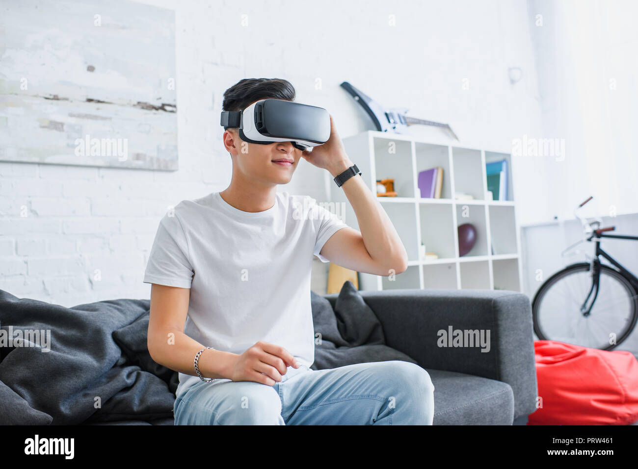 smiling young asian man using virtual reality headset while sitting on couch at home Stock Photo