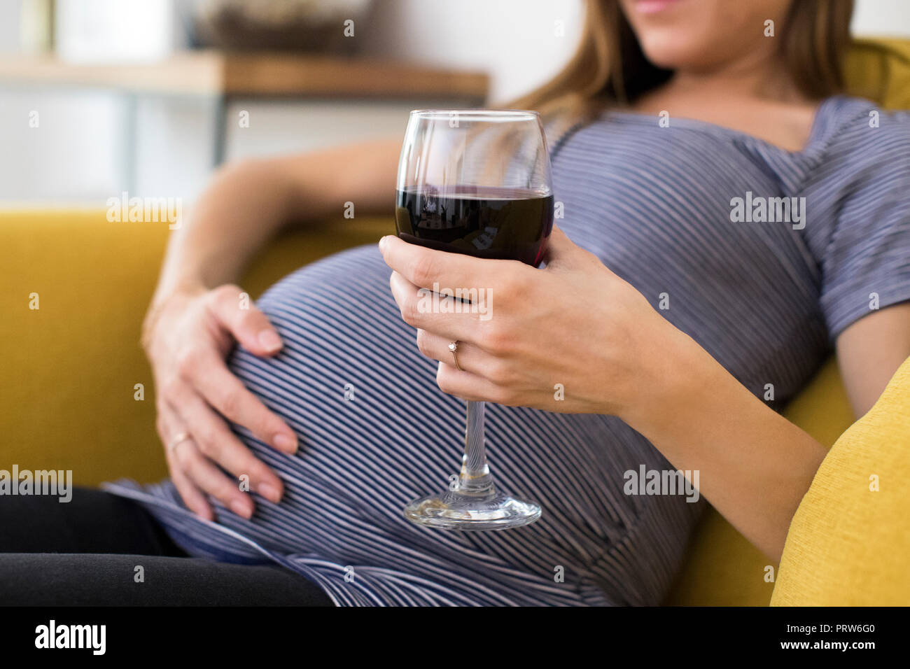 Close Up Of Pregnant Woman Drinking Red Wine Sitting On Sofa At Home Stock Photo