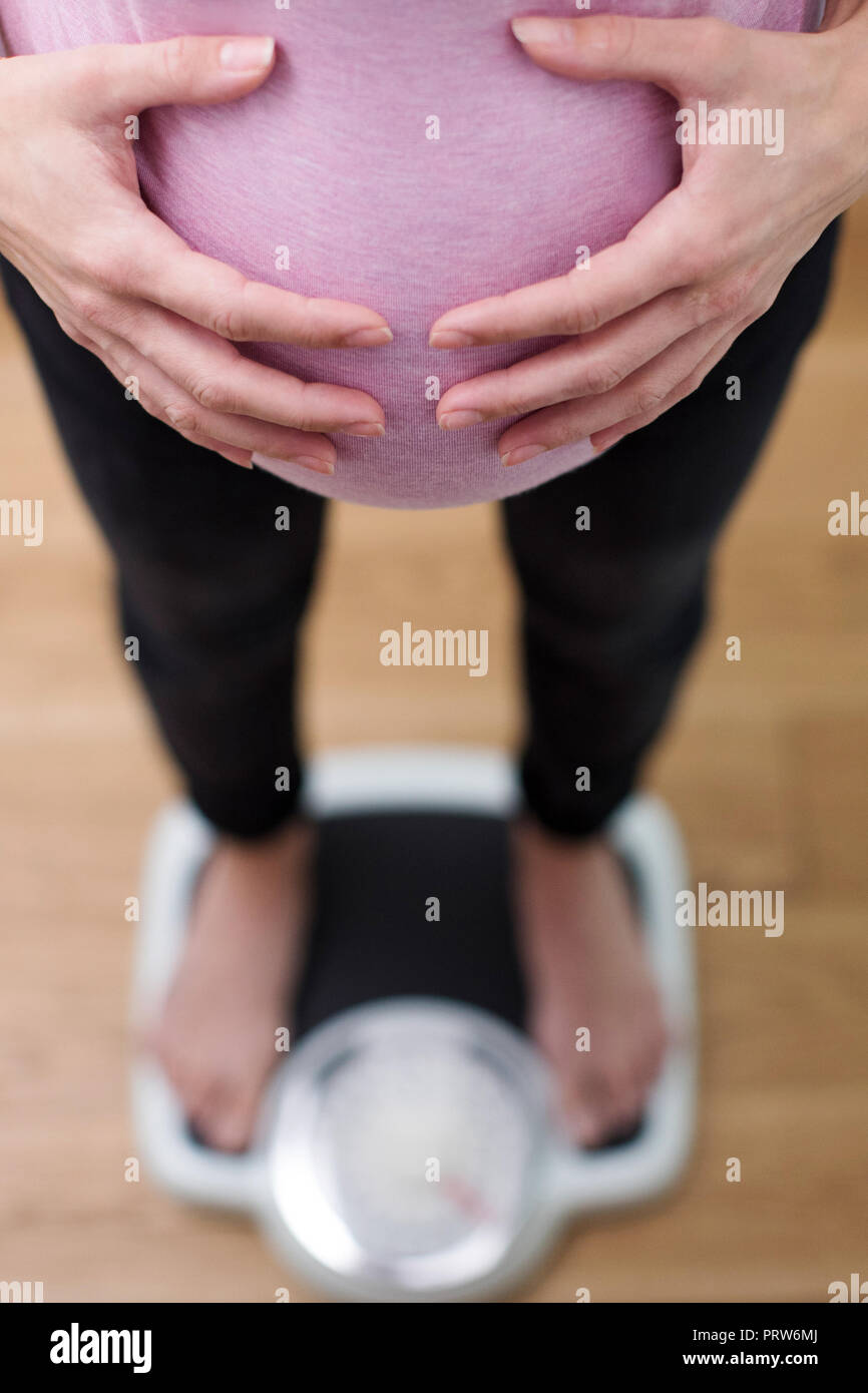 Close Up View Looking Down On Pregnant Woman Standing On Bathroom Scales Stock Photo