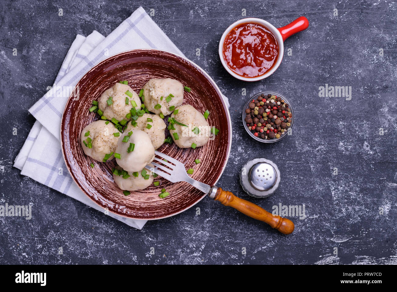Georgian dumplings Khinkali with meat, green onion and tomato sauce. Served on brown ceramic plate with bowl of sauce, pepper mix and salt. Dark concr Stock Photo