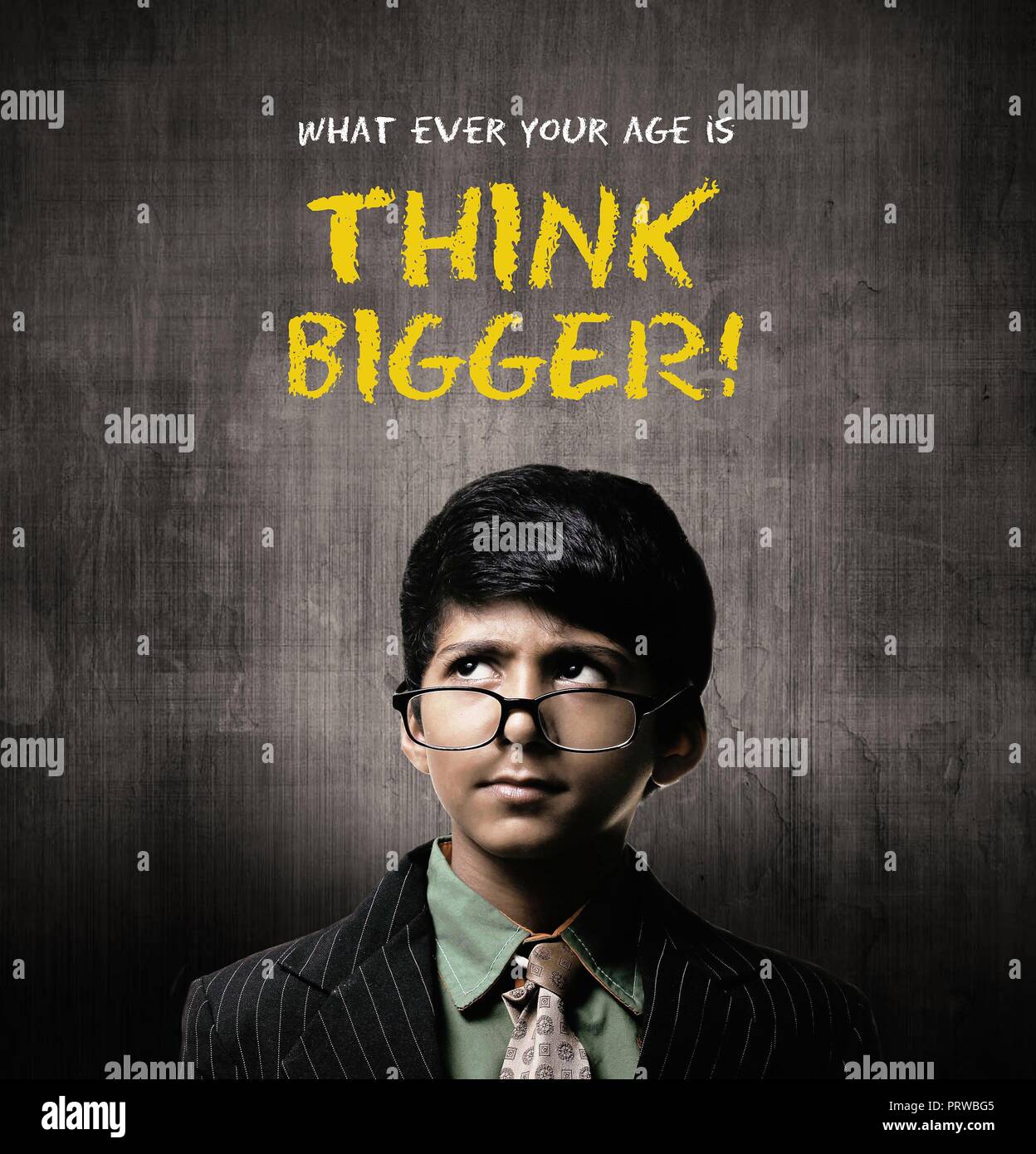 Cute Intelligent Little Boy Wearing Glasses On Nose, Thinking While Standing Before A Chalkboard, Think Bogger Written On Chalkboard Stock Photo