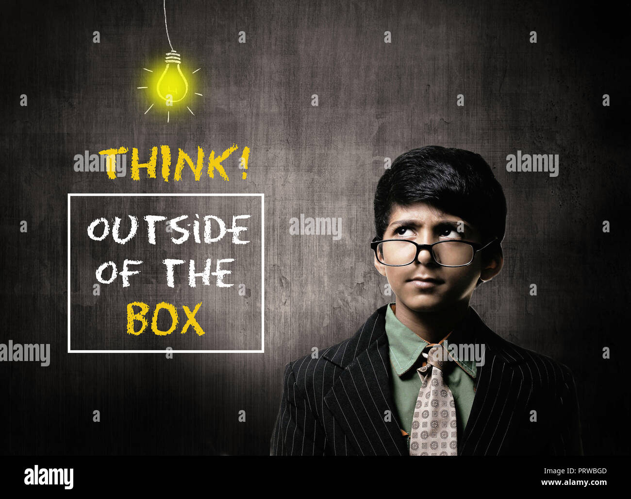 Cute Intelligent Little Boy Wearing Glasses On Nose, Thinking While Standing Before A Chalkboard, Think Outside Of The Box Written On Board Stock Photo