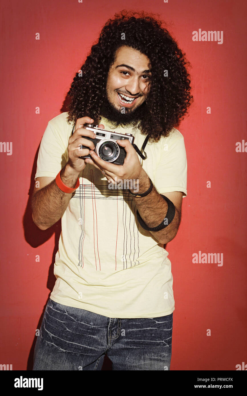 Closeup of one handsome passionate expressive cool young brunette photographer men with long curly hair holding a vintage SLR camera standing against  Stock Photo