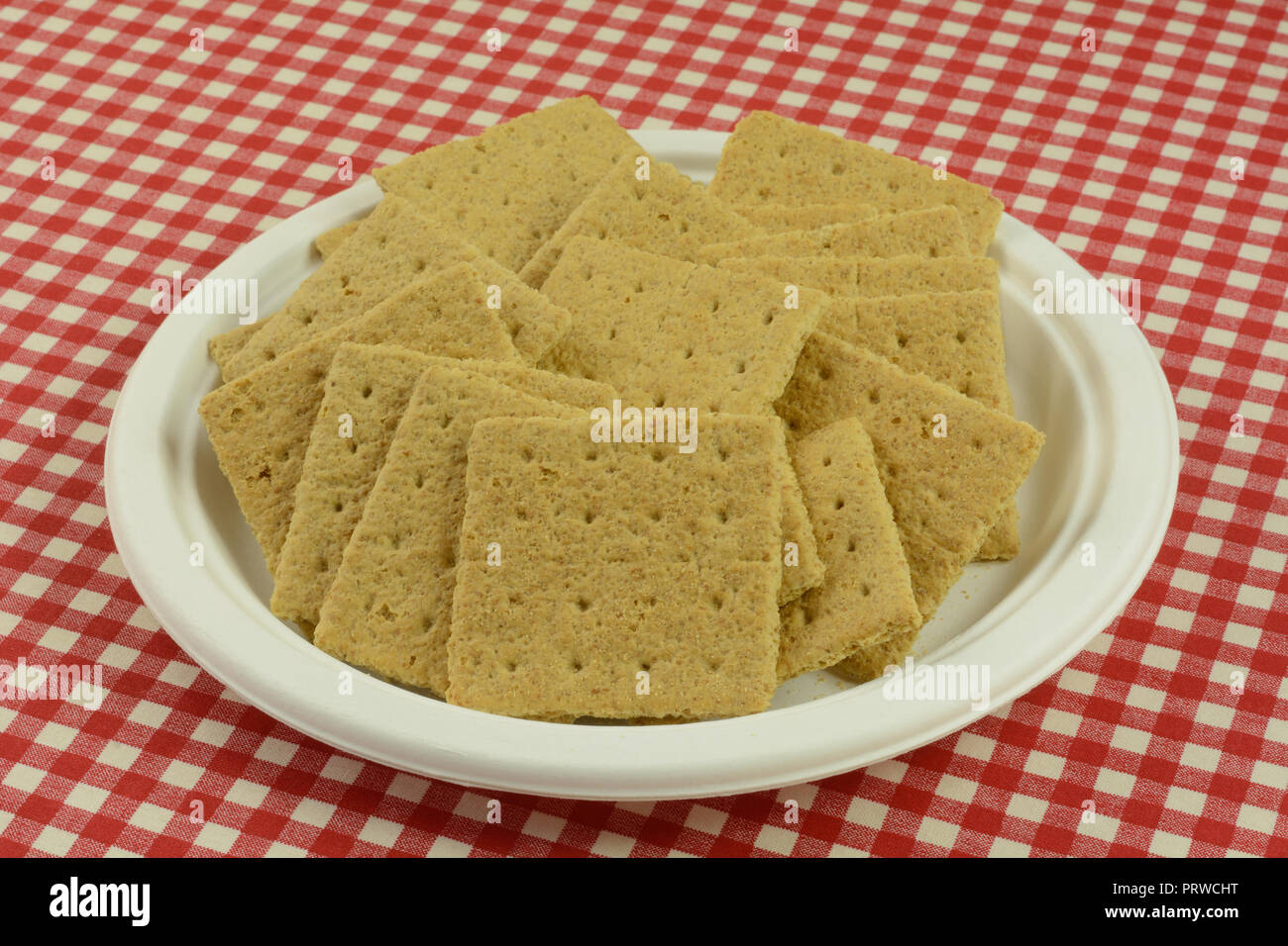 Graham cracker squares snack on white eco-friendly disposable plate in red checkered tablecloth Stock Photo