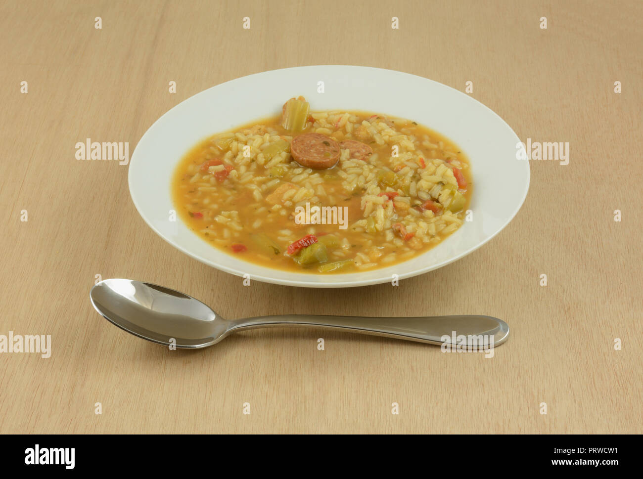Chicken sausage gumbo soup with rice and vegetables in white soup bowl with large soup spoon on wooden table Stock Photo