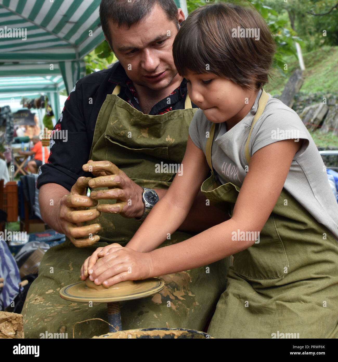 Open-air pottery workshop for children during Etara folk festival. A potter craftsman shows a small girl how to work with clay and pottery wheel Stock Photo