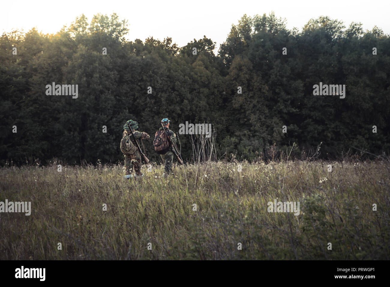 Hunting hunters in  rural field nearby forest at sunset during hunting season Stock Photo