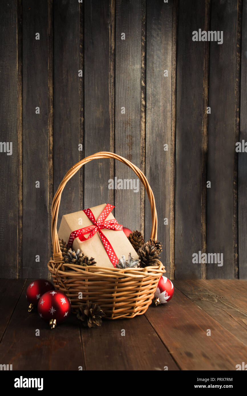 Christmas gif in craft paper with red ribbon in wicker basket with copy space on wooden background, vertical; shot Stock Photo