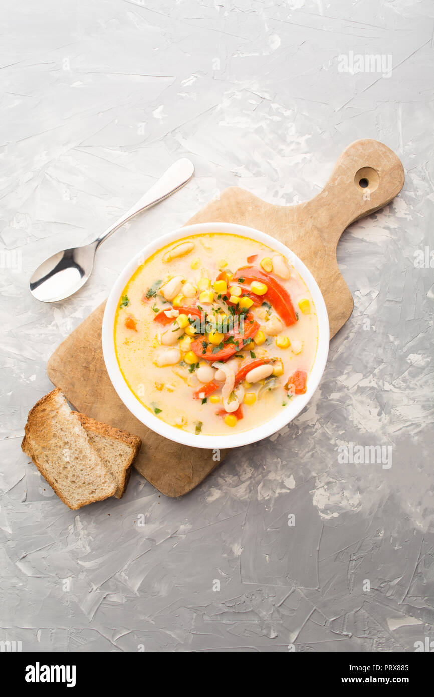 Succotash, cream soup with beans, corn and bell peppers with toast bread over wooden board on grey background, overhead view Stock Photo