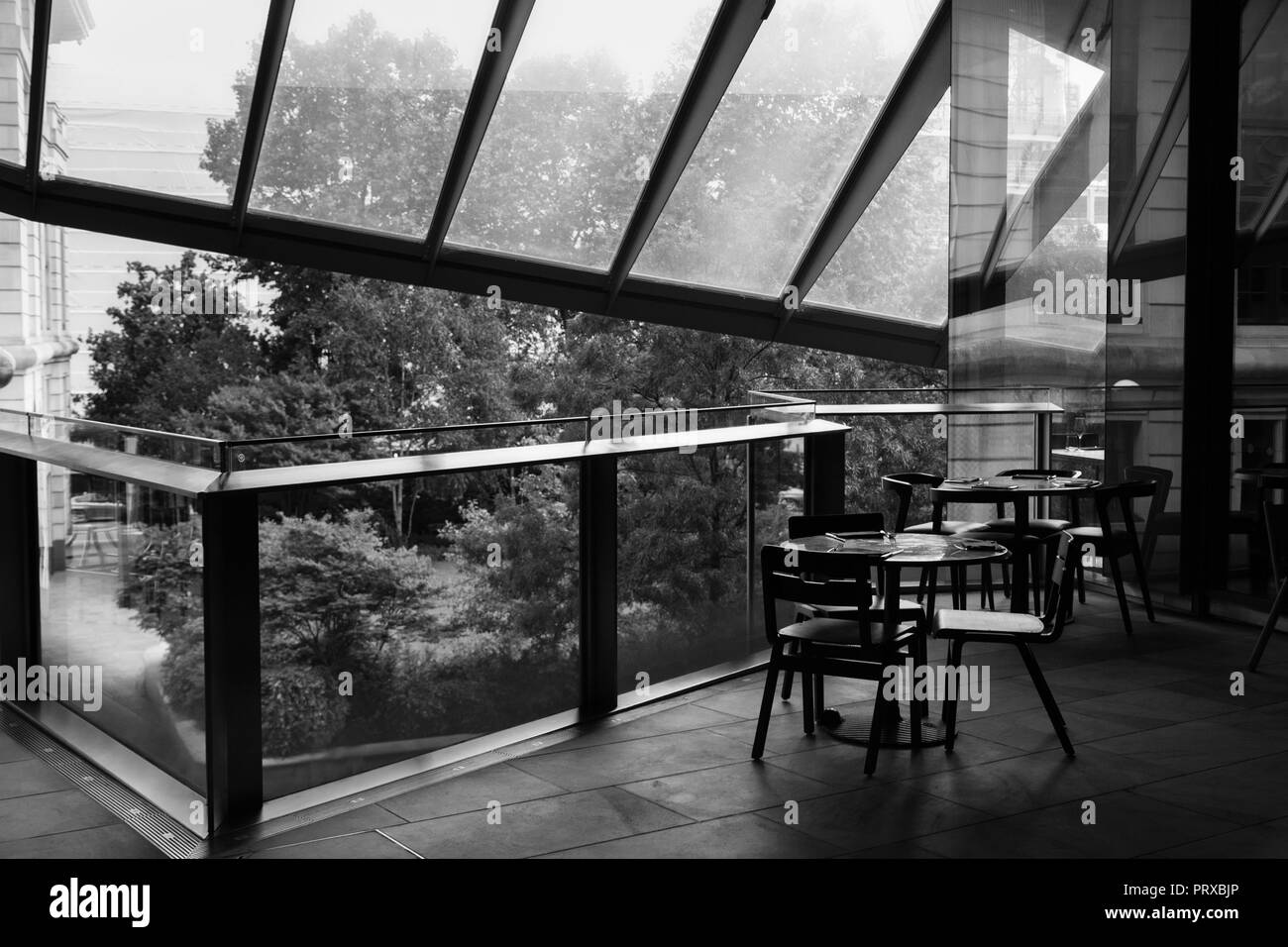 black and white picture of cafe table and chairs standing on a balcony of a trade center under a glass roof Stock Photo