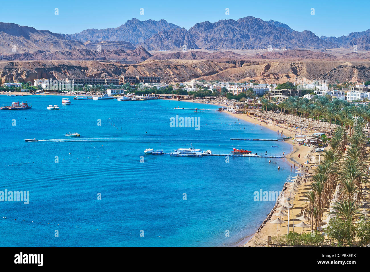 The cozy sand beach of Sharm El Maya is lined with shady palm trees and surrounded by Sinai desert rocks, Sharm El Sheikh, Egypt. Stock Photo