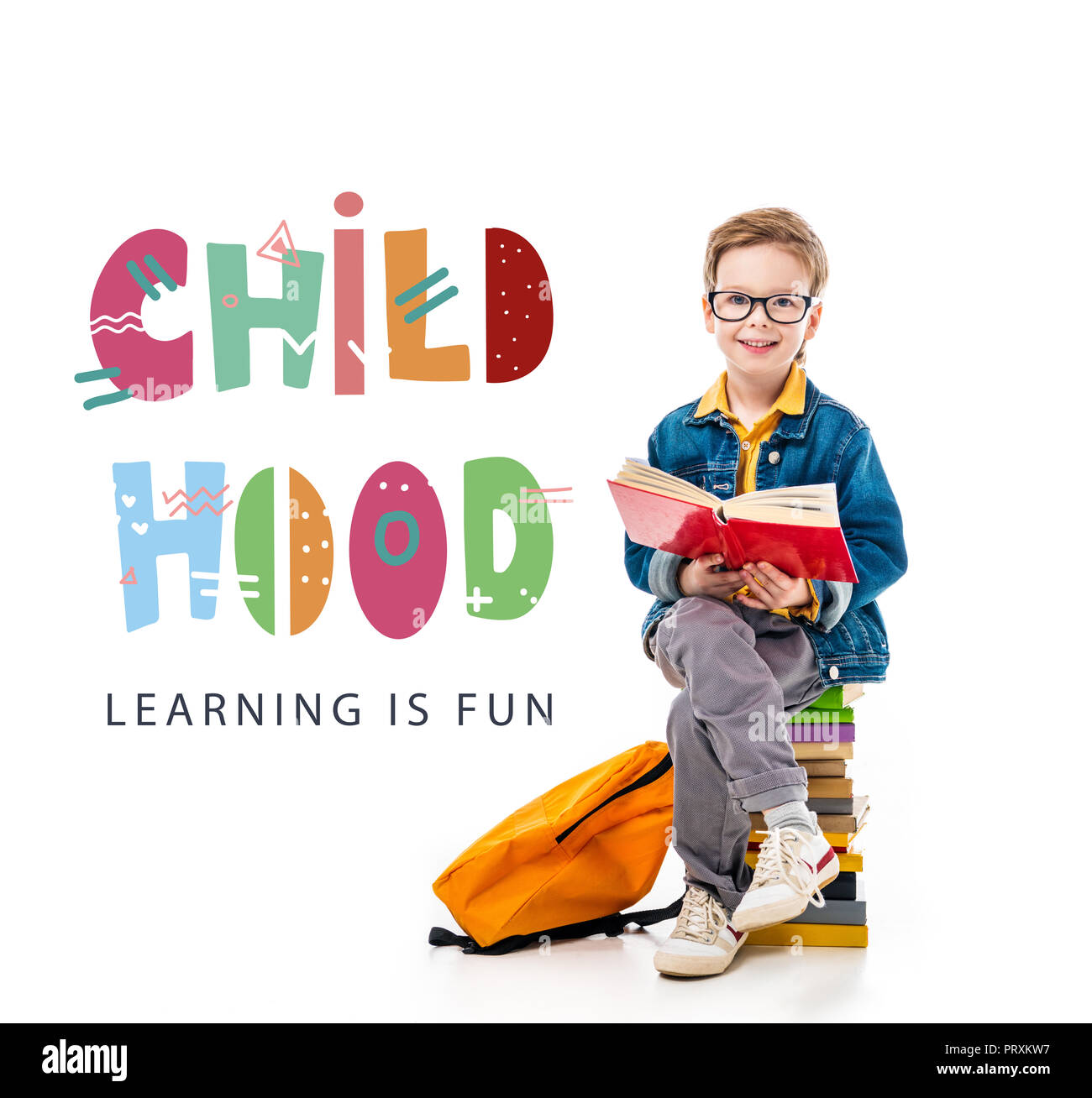 cheerful schoolboy reading book and sitting on pile of books with ...