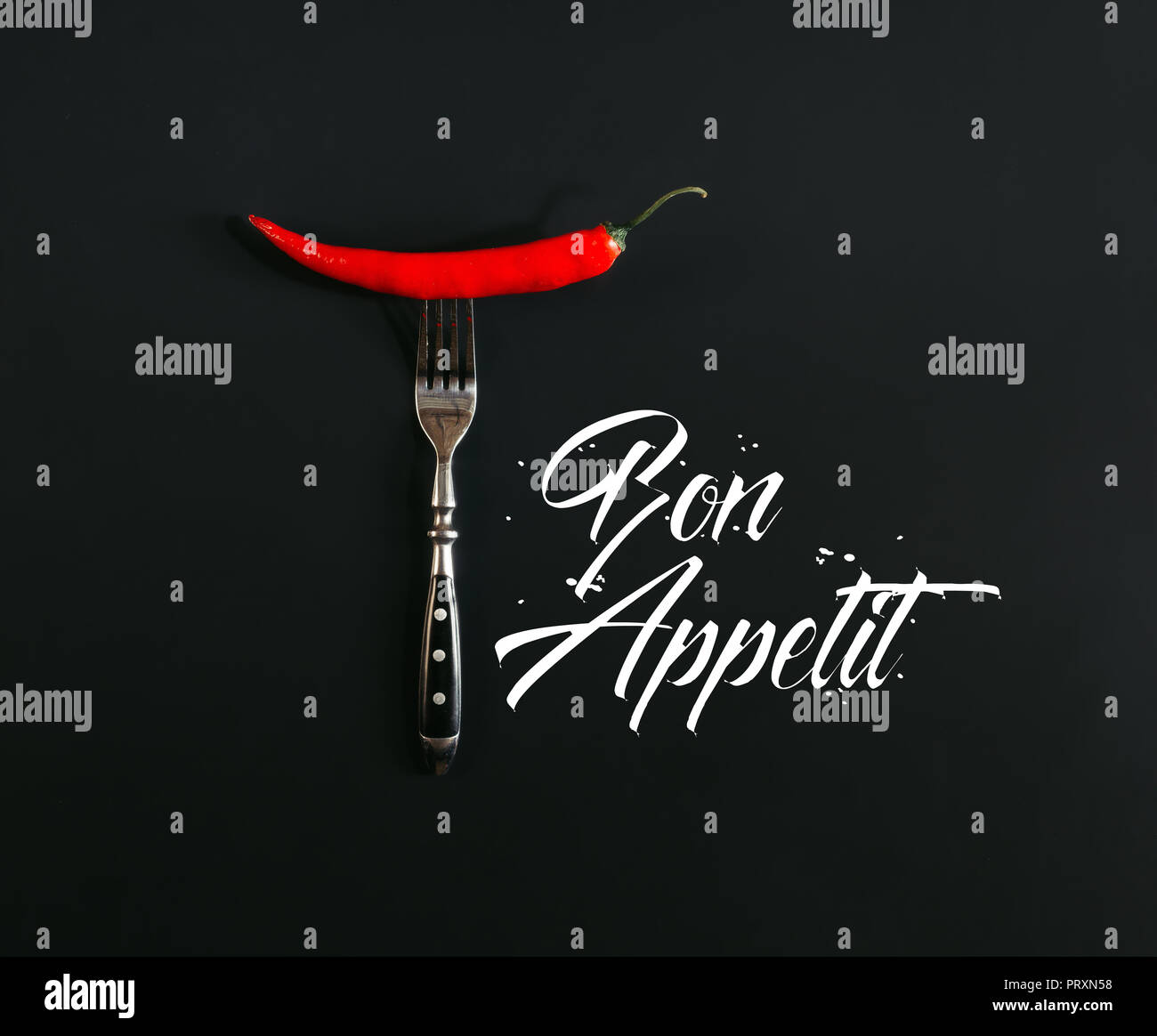 red hot chili pepper on fork on black with 'bon appetit' lettering Stock Photo