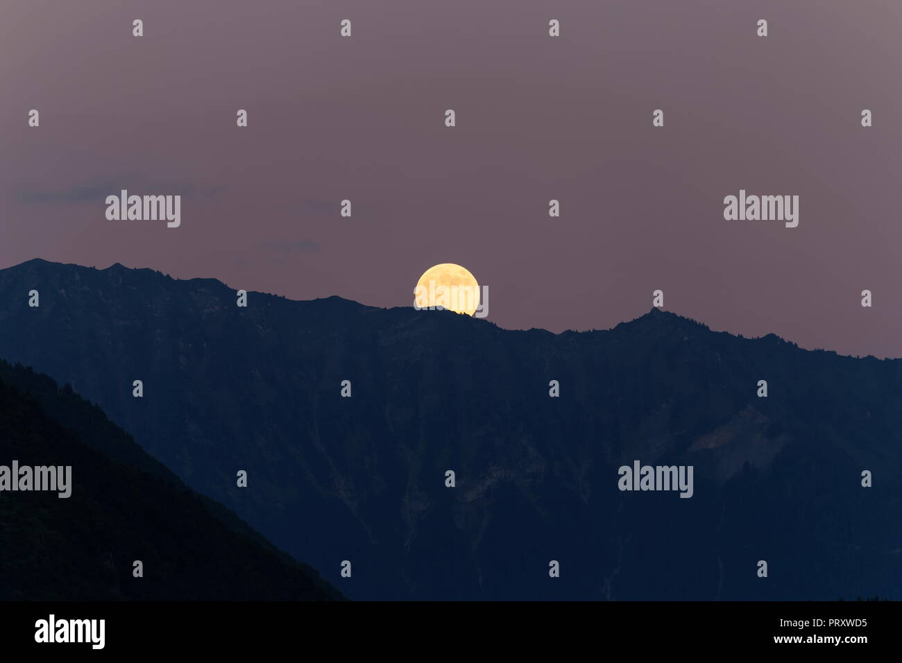 Orange full moon rising over the mountains nr Faverges France Stock Photo