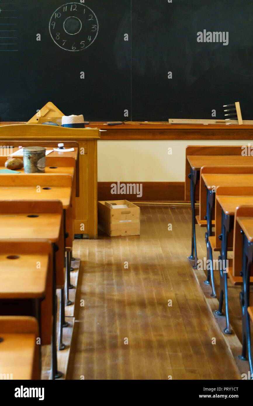 Empty desks at school classroom with chalkboard at the background. Stock Photo