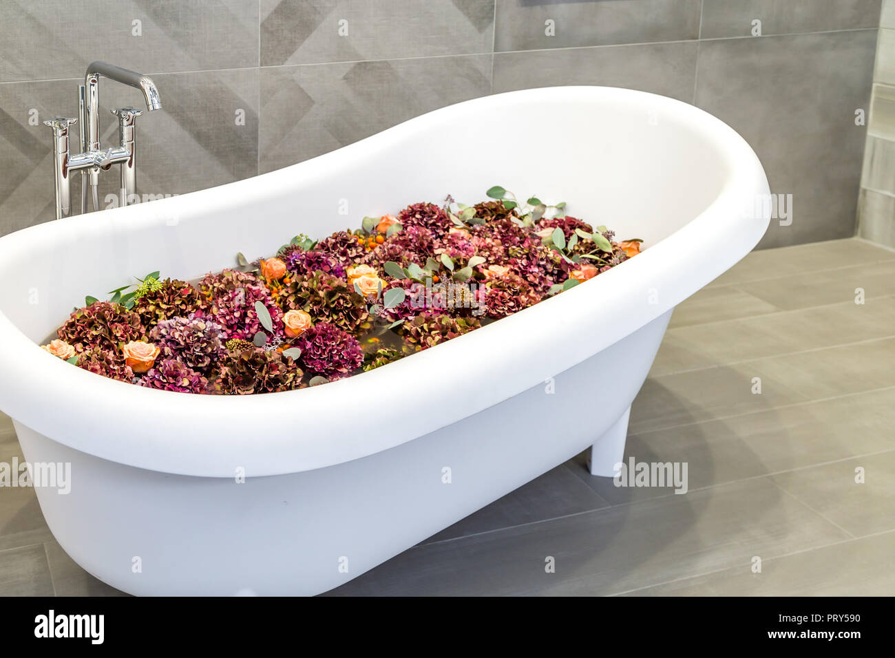 Flowers potpourri floating in the water of a white bathtub Stock Photo
