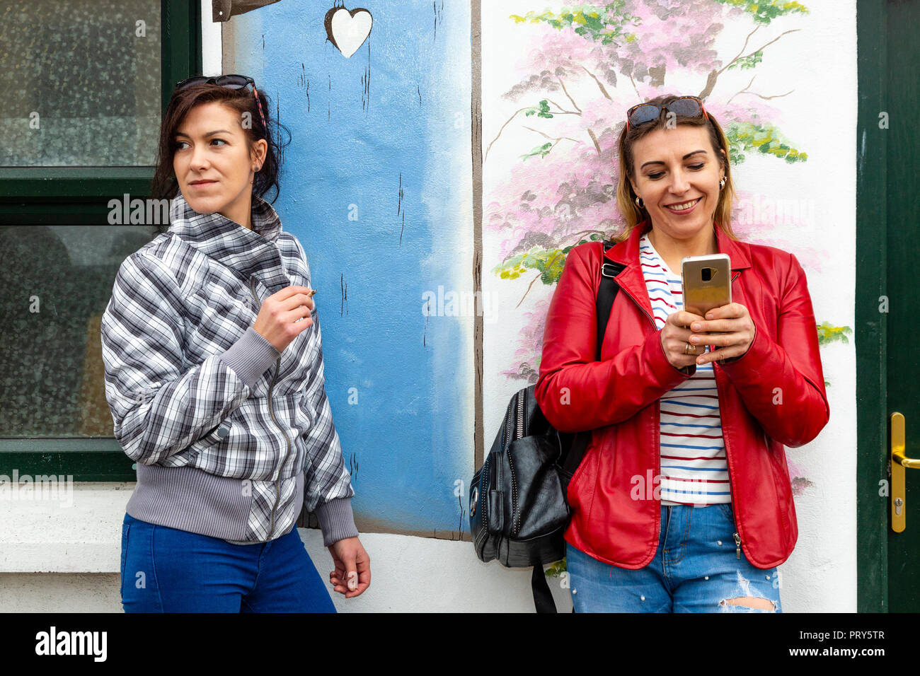 Two women smoking and using smartphone on Street Stock Photo