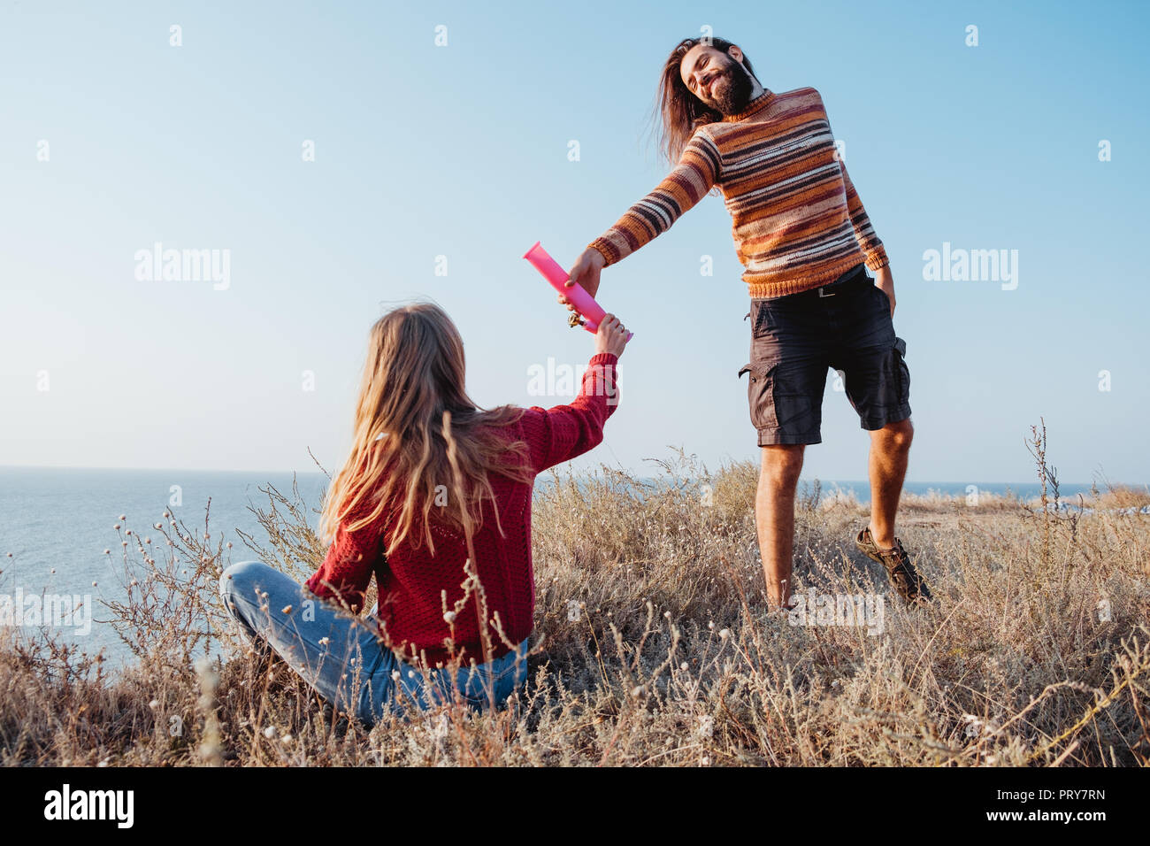 Rebel hipster woman and man friends passing each other a pink water bong outdoors. Stock Photo