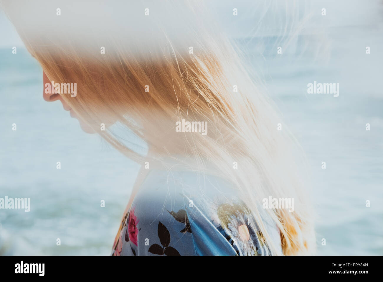 Close-up ortrait of a young beautiful graceful and naturally blond woman in blue dress with sea in background Stock Photo