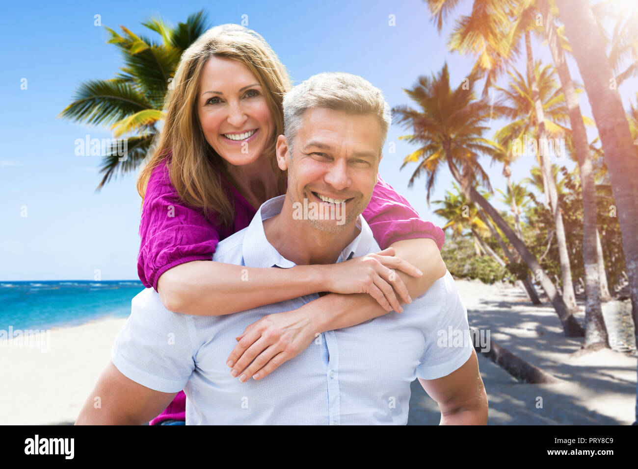 Portrait Of A Smiling Mature Man Giving Piggyback To His Wife At Beach Stock Photo