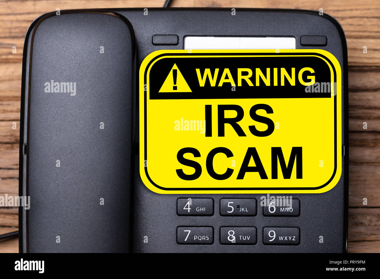 Elevated View Of IRS Scam Warning Sign On Black Landline Phone Stock Photo