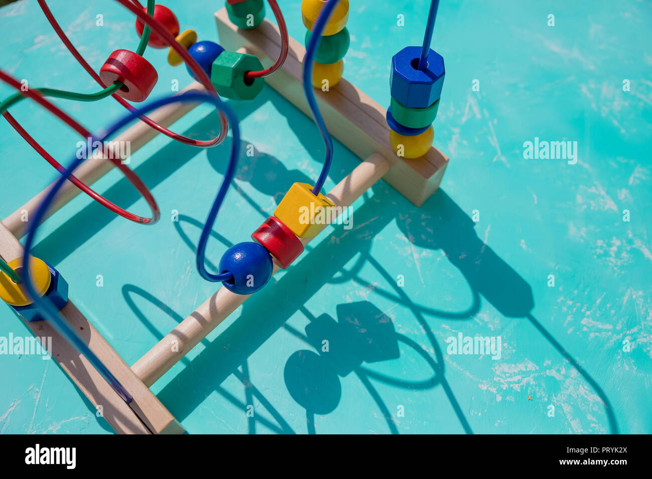 Children's toy labyrinth, maze on a metal spiral with ball, cylinder, cube on a wooden stand close-up.learning color and form in various shapes. Develops fine motor skills and logical thinking.Copy space Stock Photo