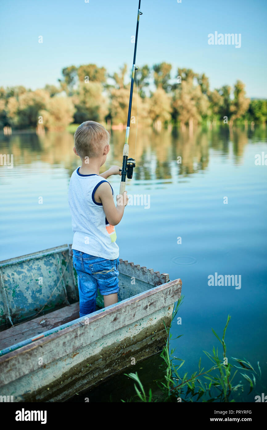 Back view of little boy with fishing rod standing in boat Stock Photo