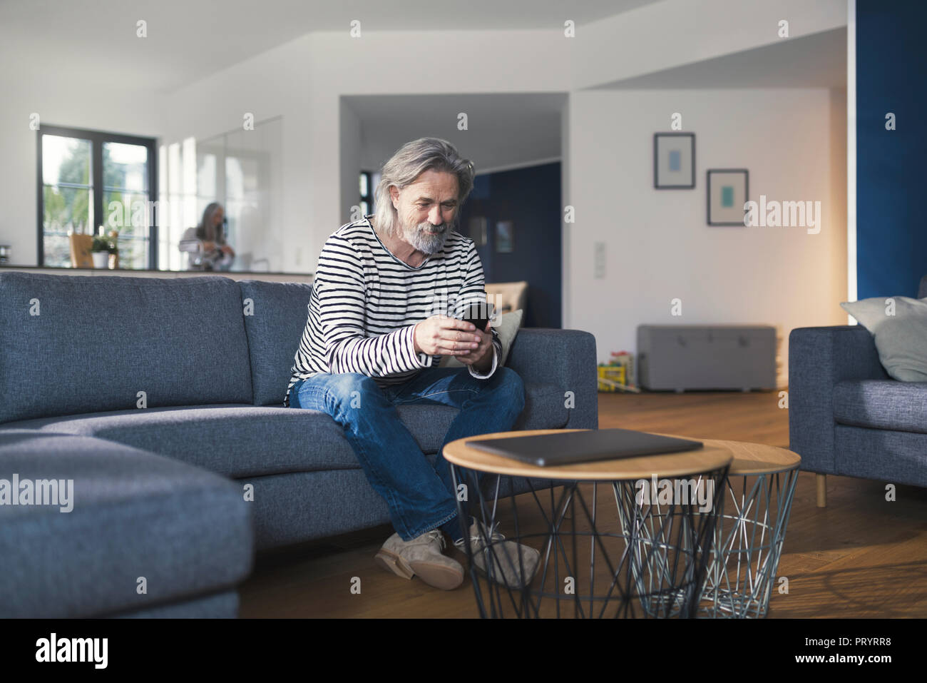 Senior man sitting on couch, using smartphone Stock Photo