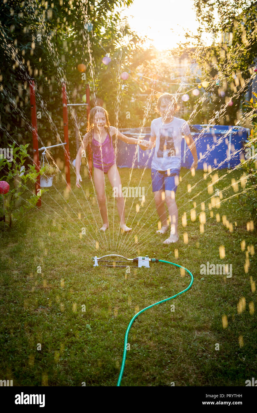 Brother and sister having fun with lawn sprinkler in the garden Stock ...