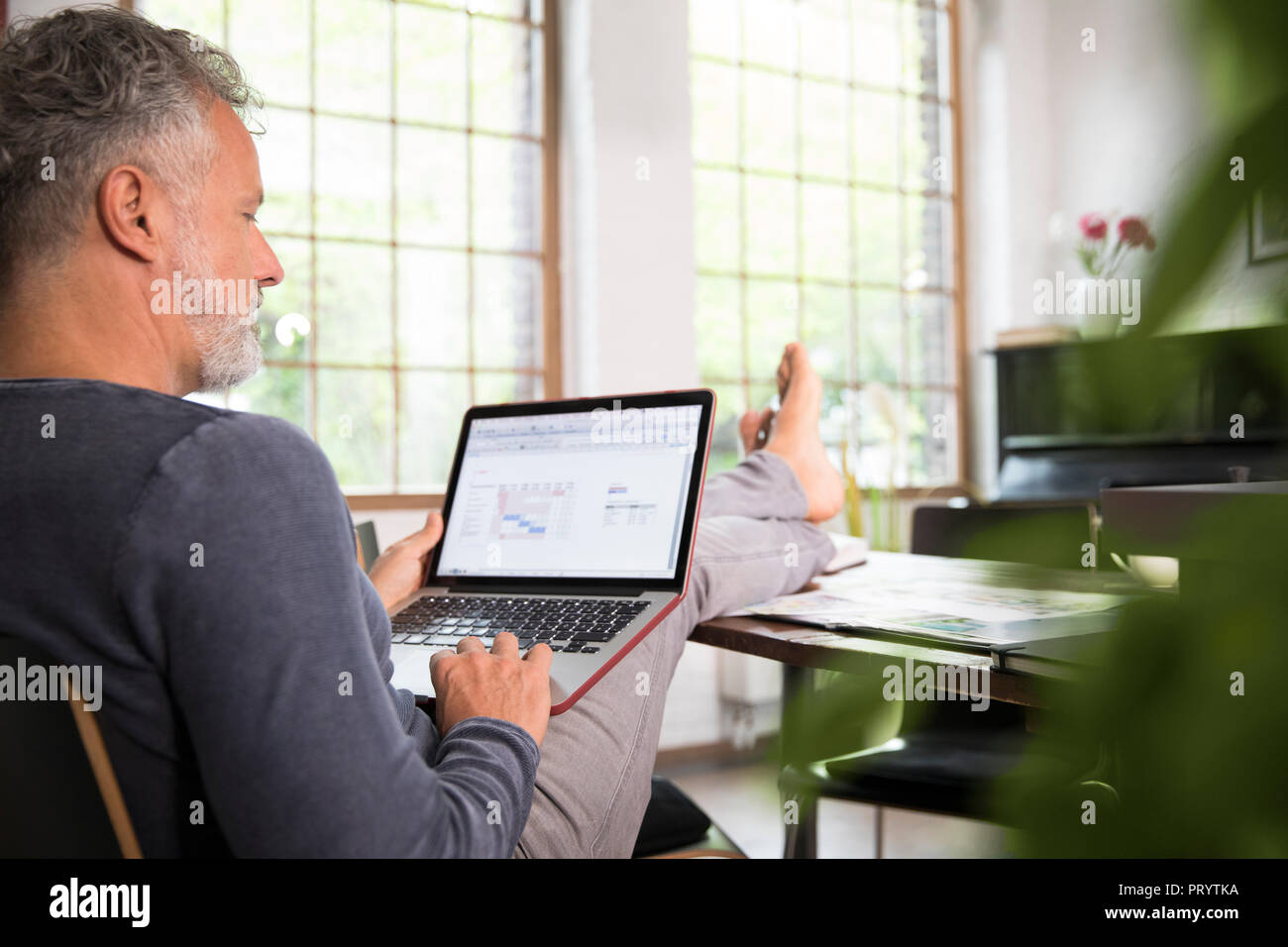 Mature man working from his home office with feet up, using laptop Stock Photo