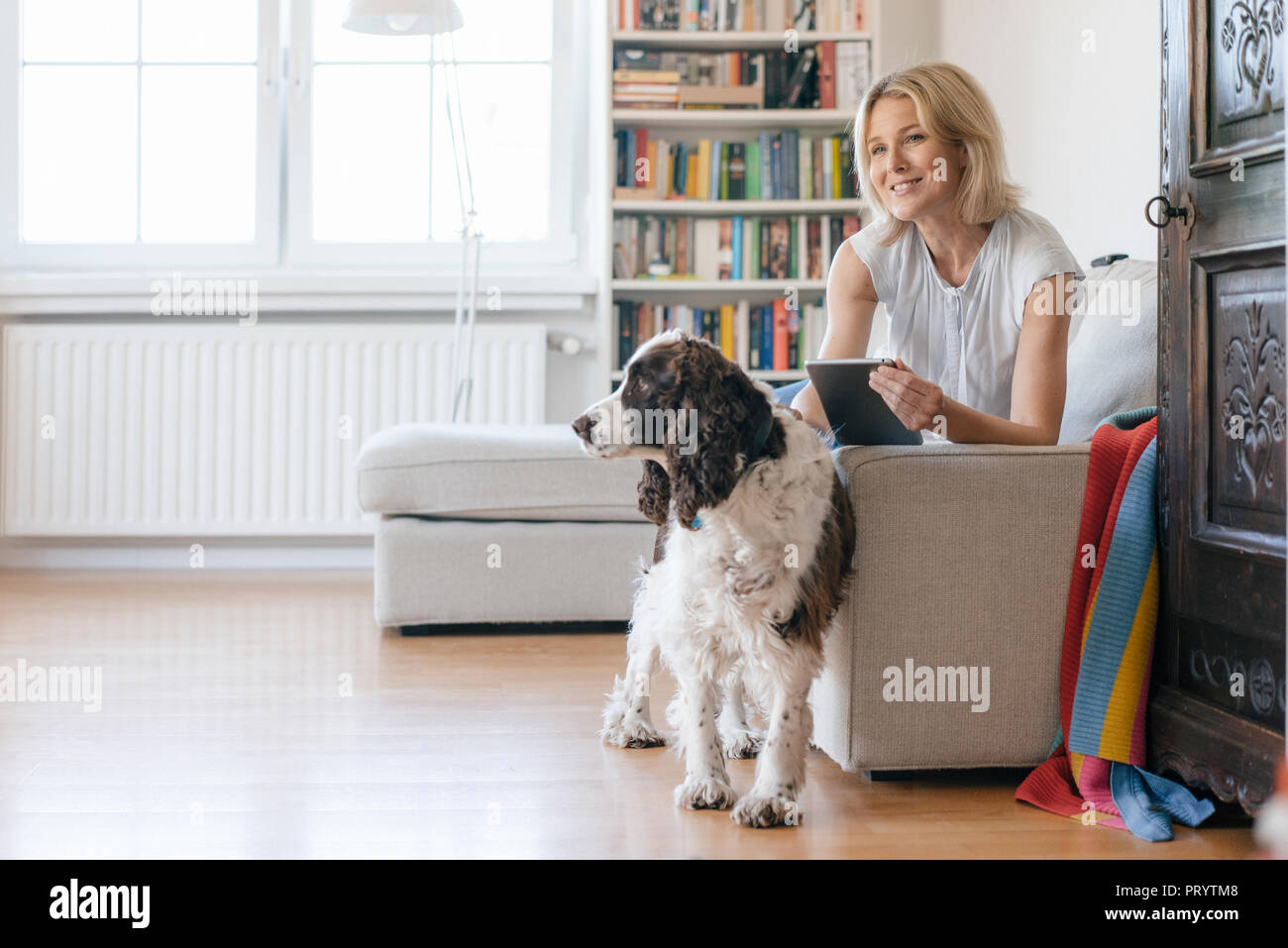 Smiling mature woman with dog lying on couch at home holding tablet Stock Photo