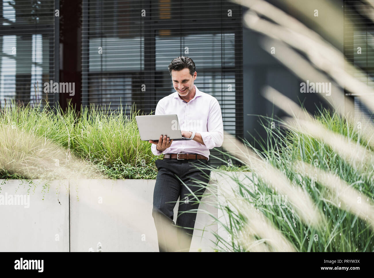 Smiling businessman using laptop outside office building Stock Photo