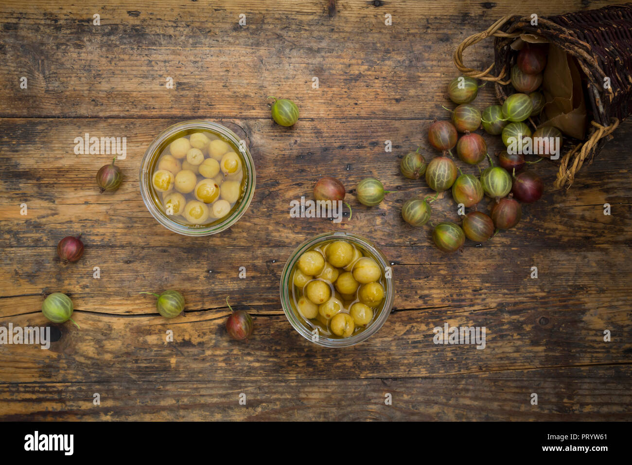 Two jars of preserved gooseberries and gooseberries on wood Stock Photo