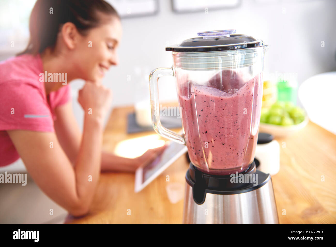 Young woman using tablet in the kitchen while preparing smoothie Stock Photo