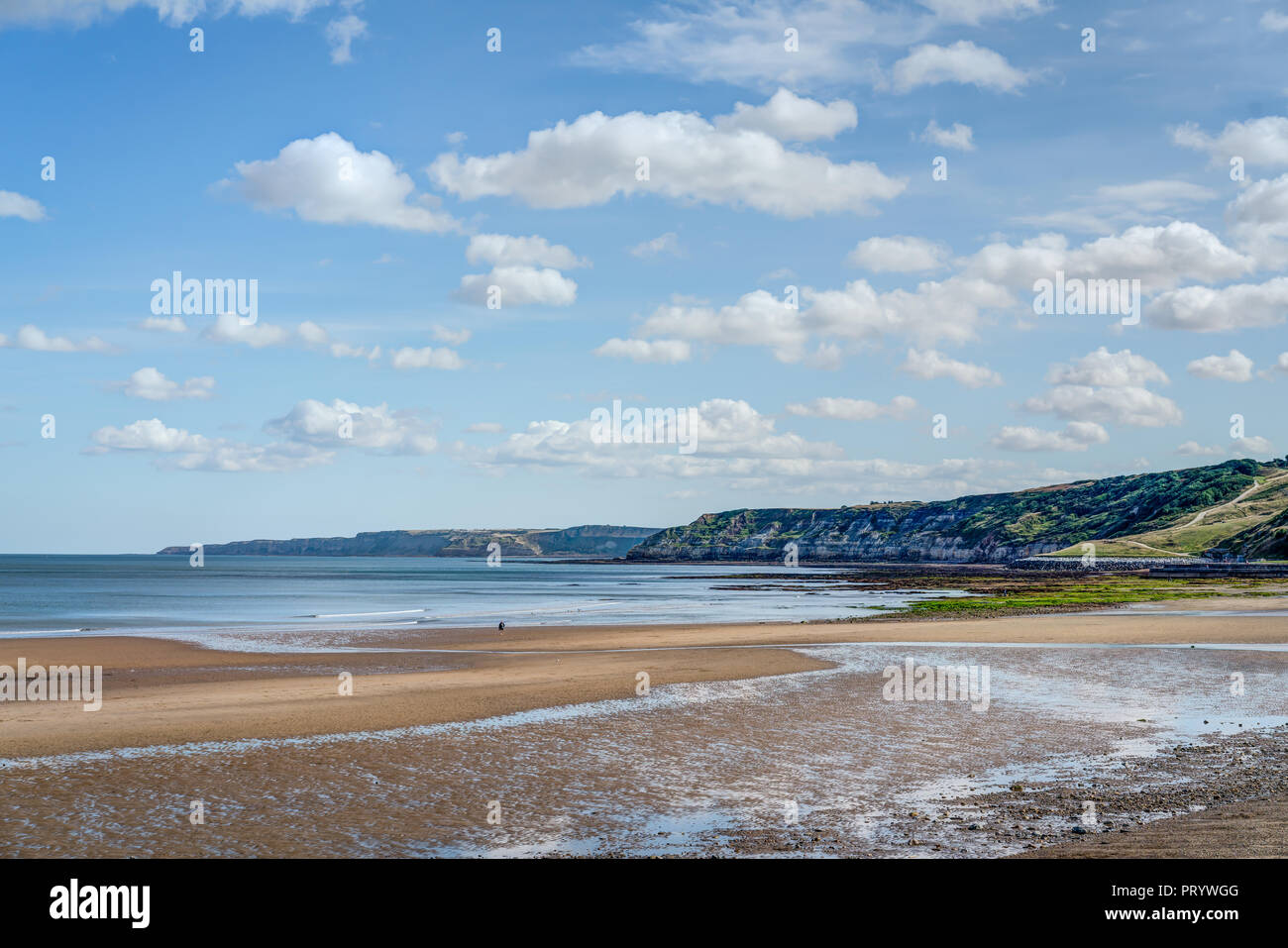 Down the south end of the sandy beach at Scarborough holiday resort looking down the rocky cliffs to Filey Brigg in the distance. Beautiful sunny day Stock Photo