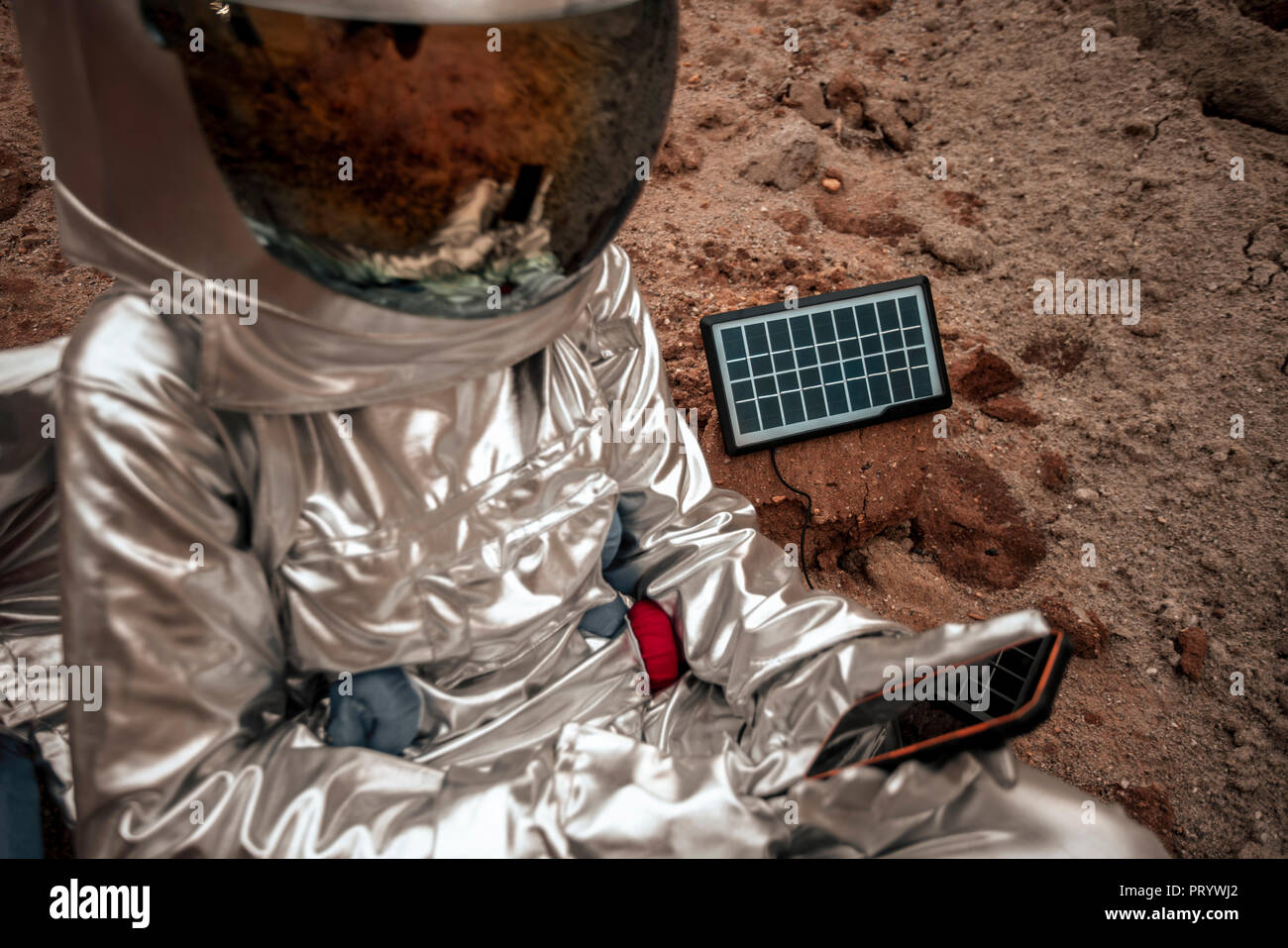 Spaceman sitting on nameless planet, charging device with solar panel Stock Photo