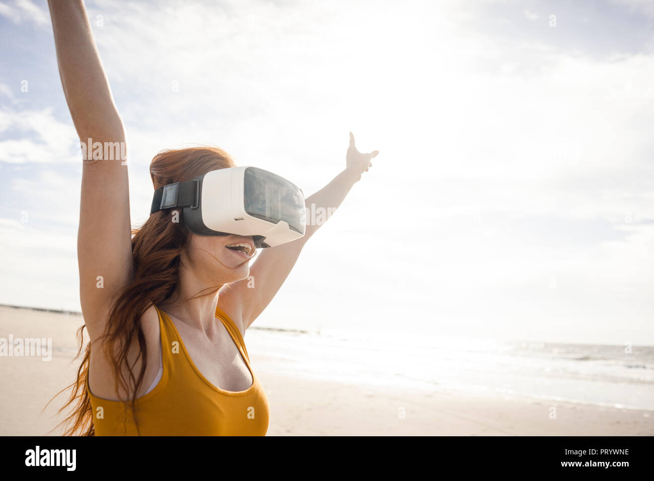 Redheaded woman using VR glasses on the beach Stock Photo