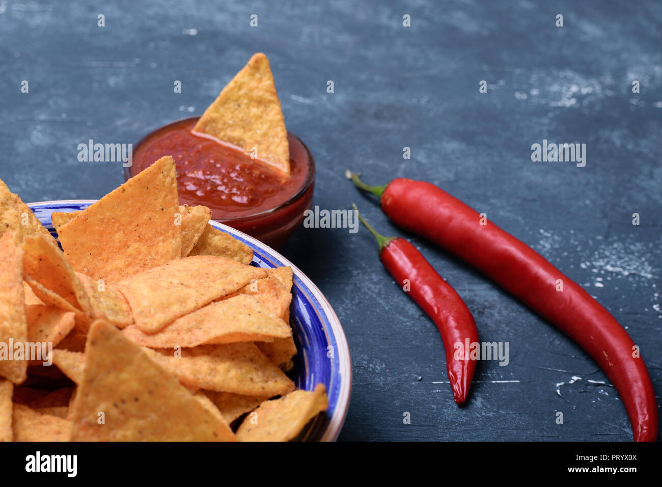 Tasty mexican tortilla chips with tomato salsa sauce on dark blue