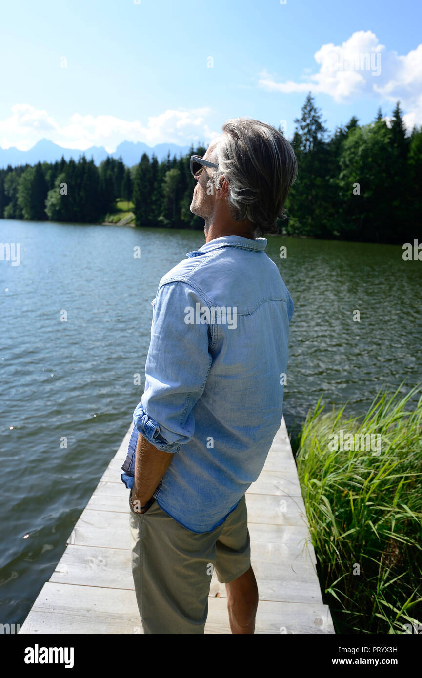 Germany, Mittenwald, mature man standing on jetty at lake relaxing Stock Photo