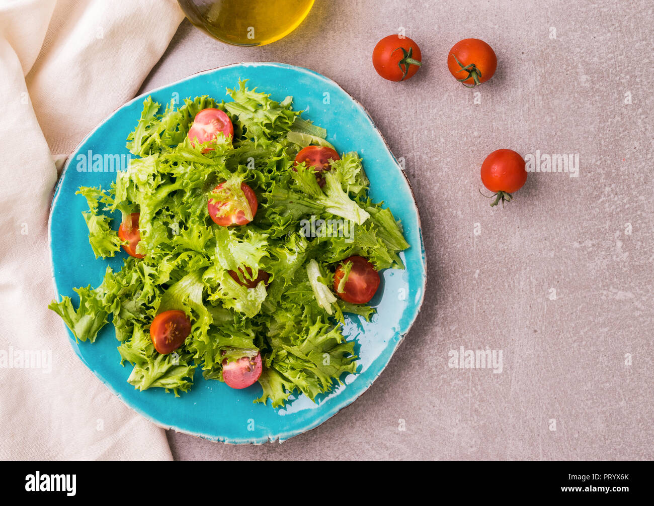 Salad with frisee and cherry tomatoes on blue ceramic plate. Healthy food concept. Top view, view from above. Light stone table background. Stock Photo