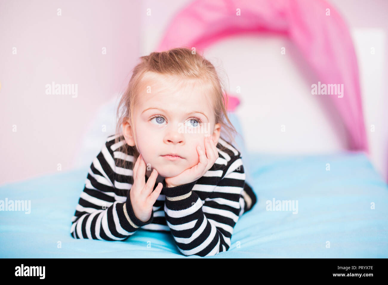 Portrait of daydreaming little girl lying on bed at home Stock Photo